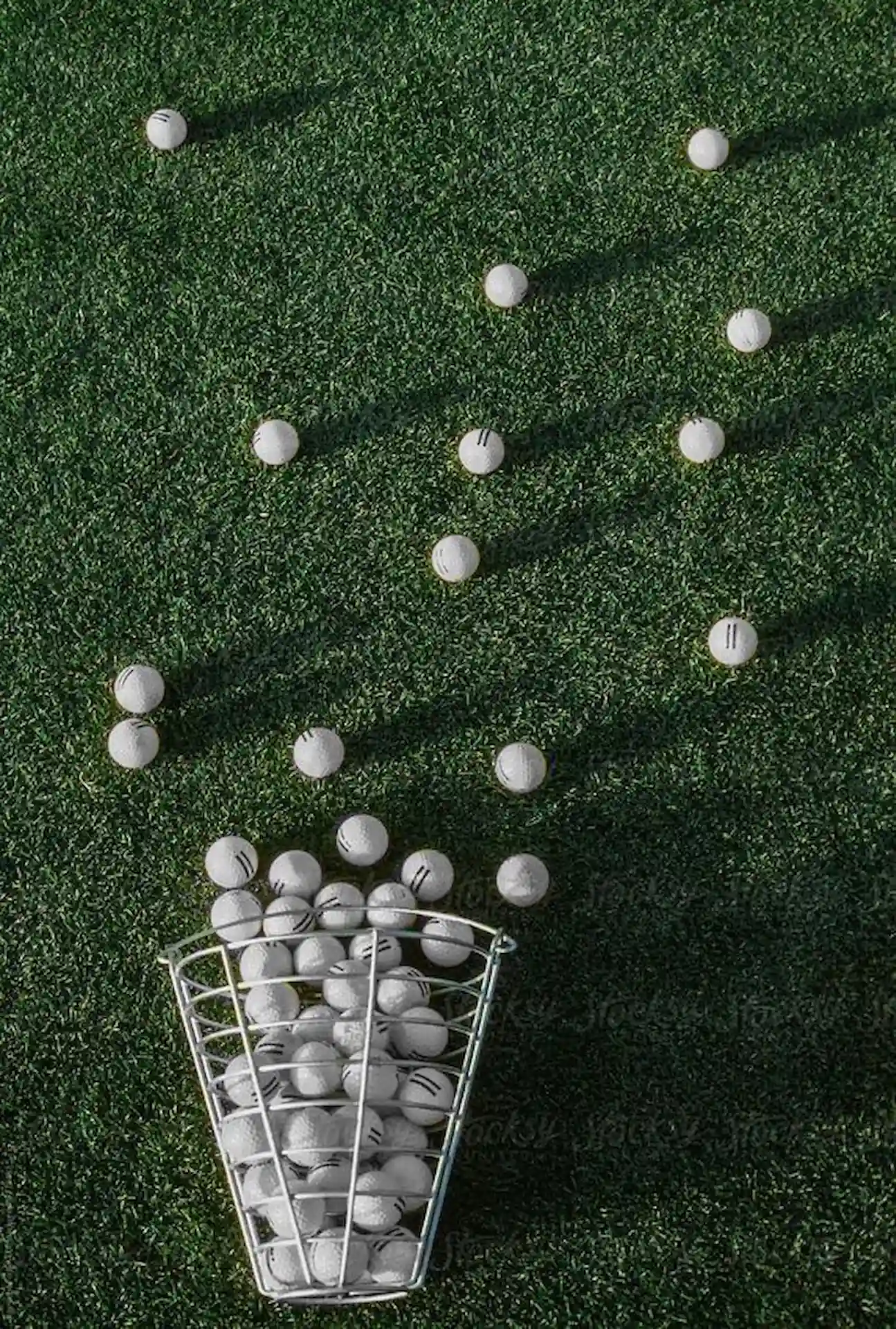 Branding by Spherical 13 Golf balls scattered on green turf beside a wire basket filled with balls.