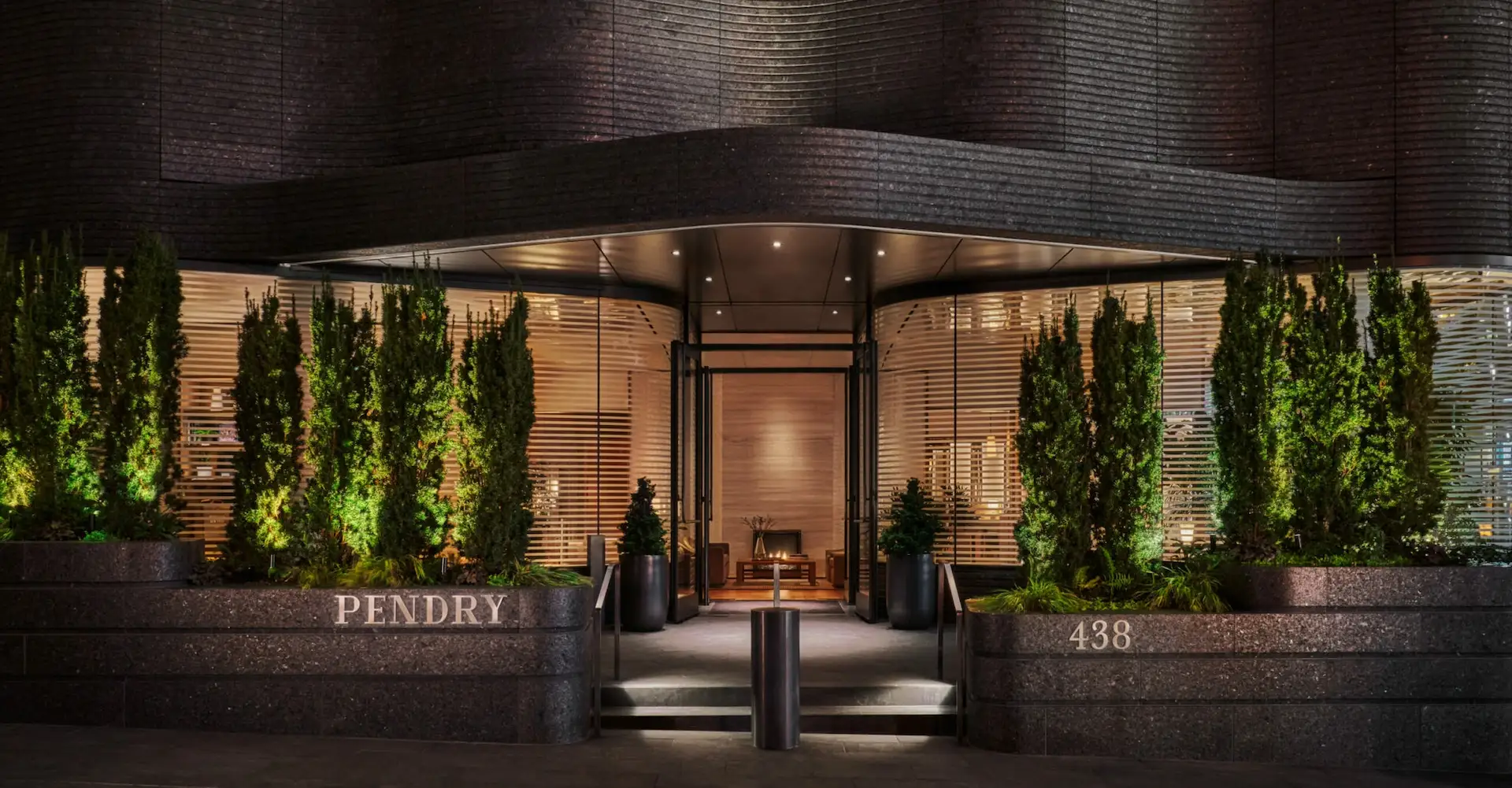 Modern luxury hotel entrance at night with illuminated greenery, glass doors, and Pendry signage on stone walls.