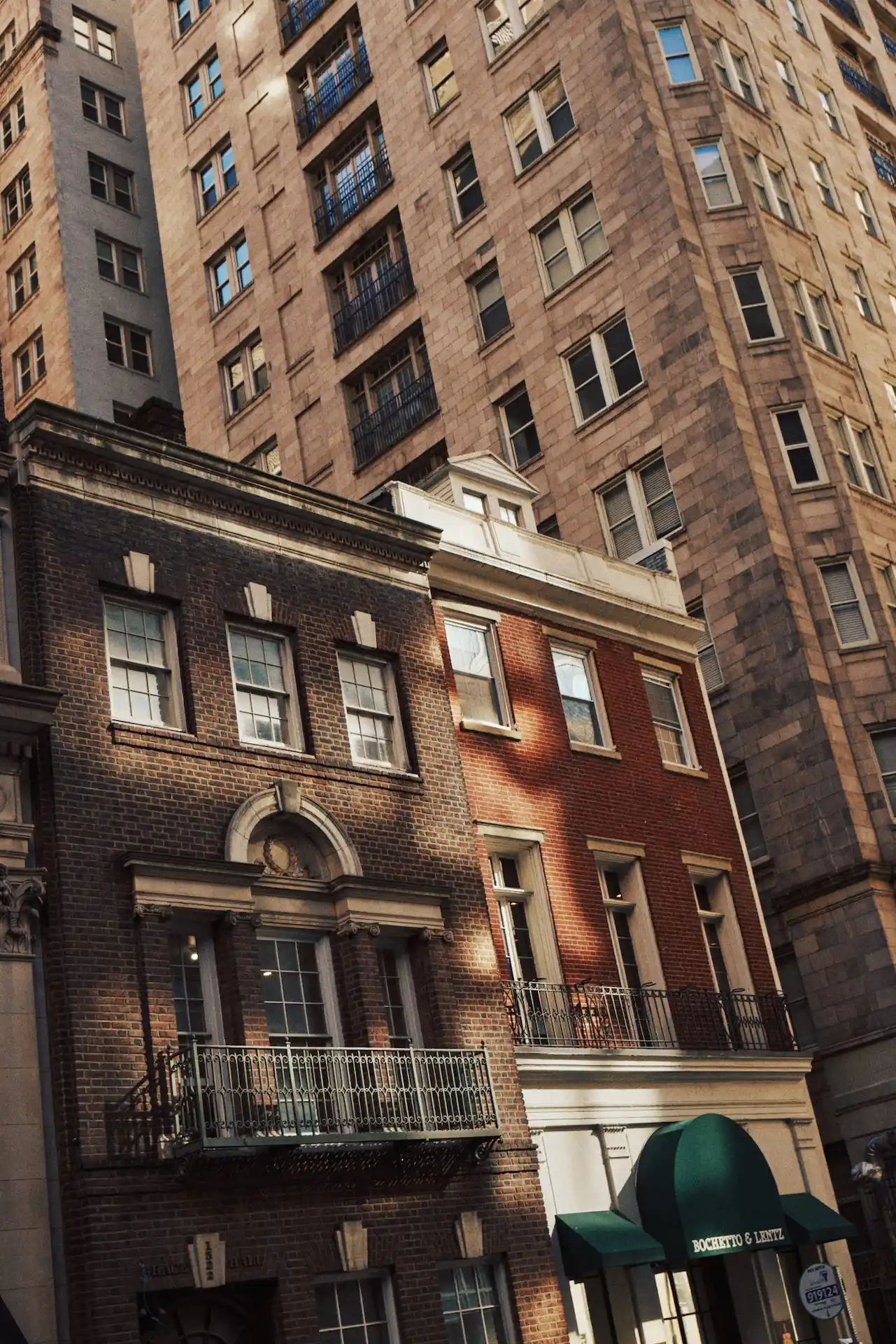 Brick buildings with classic facades and green awning contrast with modern high-rise in background.