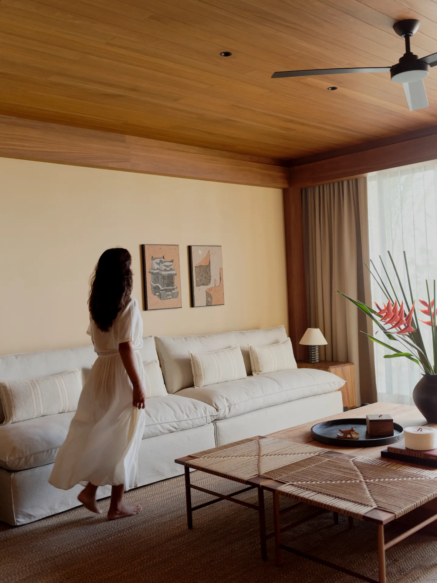 Minimalist living room at Rosewood Mandarina with woven textures, heliconia flowers, and guest in flowing white dress.