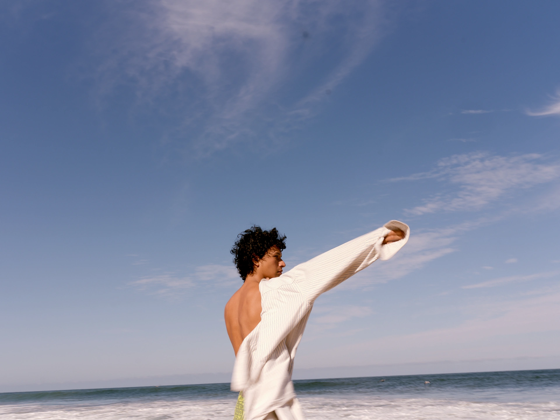 Guest on the beach at Rosewood Mandarina adjusting white top, waves and clear sky in the background.