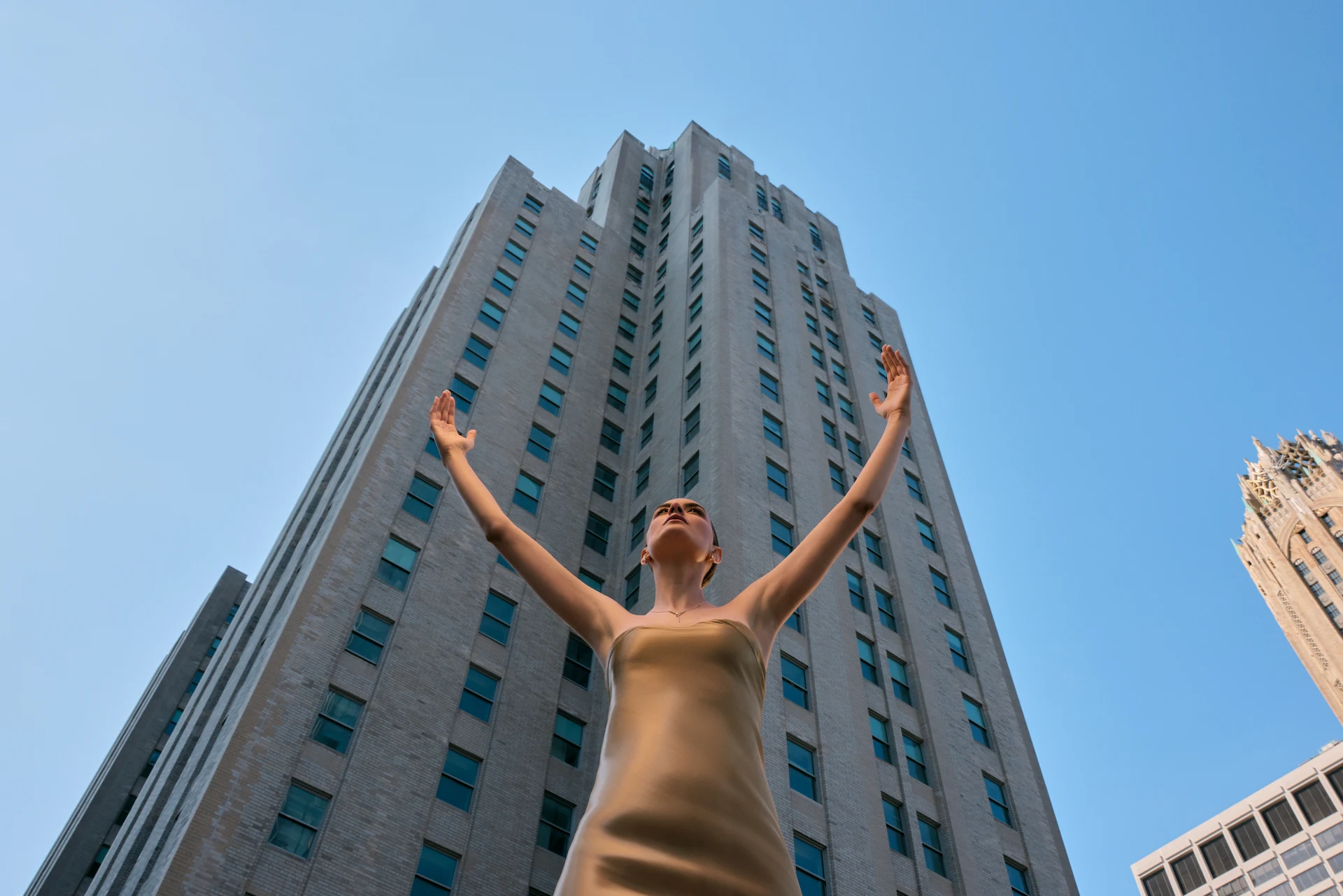 Guest raising arms beneath skyscraper at Waldorf Astoria New York, framed by clear sky and urban grandeur.