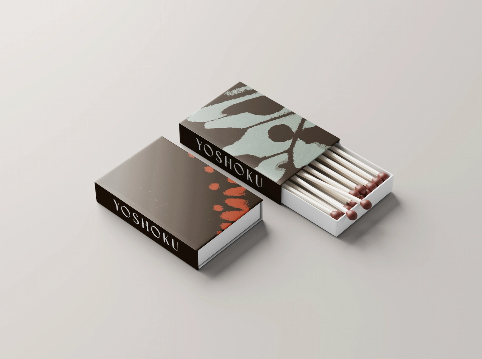 Two YOSHOKU matchboxes on light surface, one open with brown-tipped matches, both featuring abstract designs.