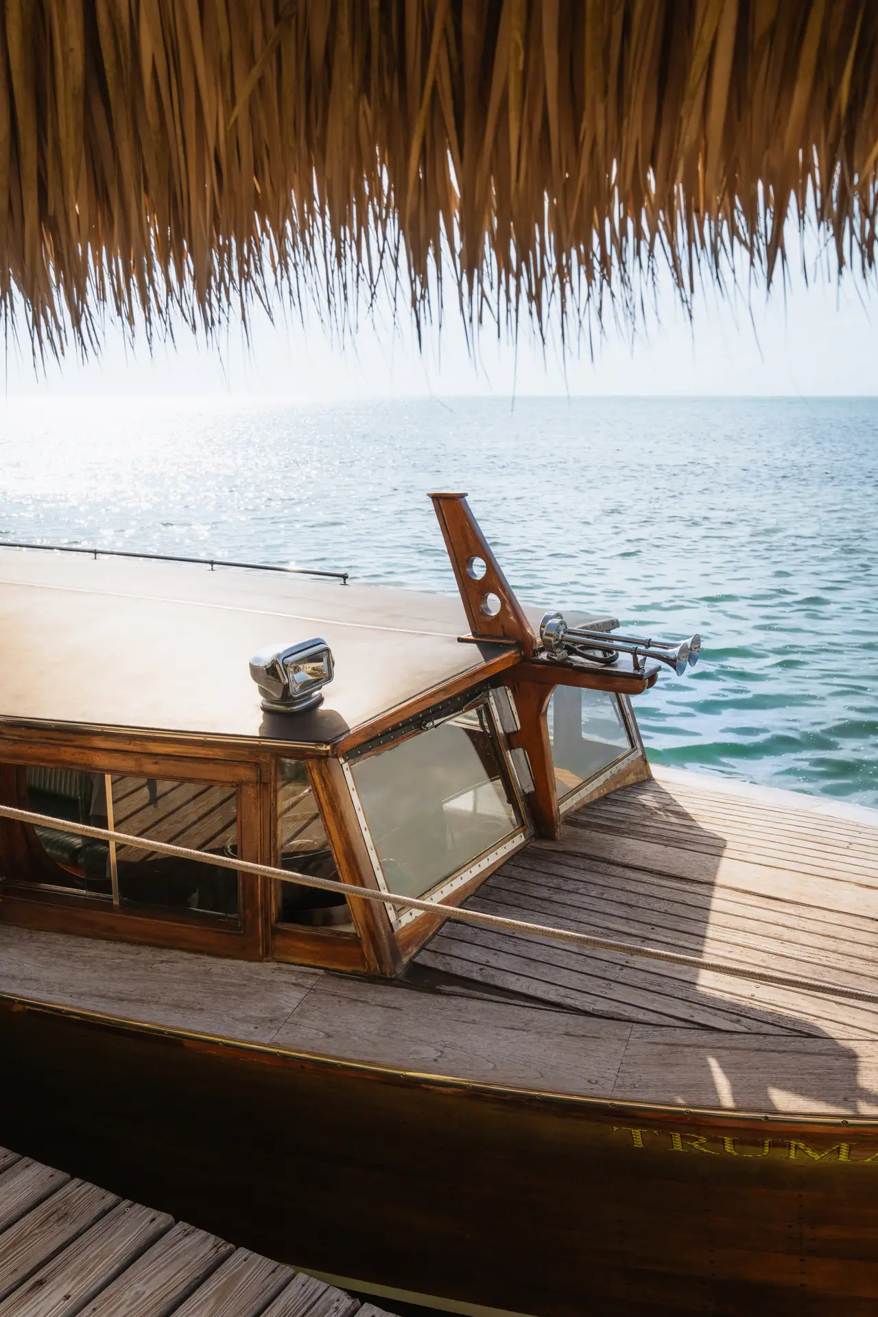 Classic wooden boat docked by the sea beneath a thatched roof, with calm ocean waters and a bright horizon.