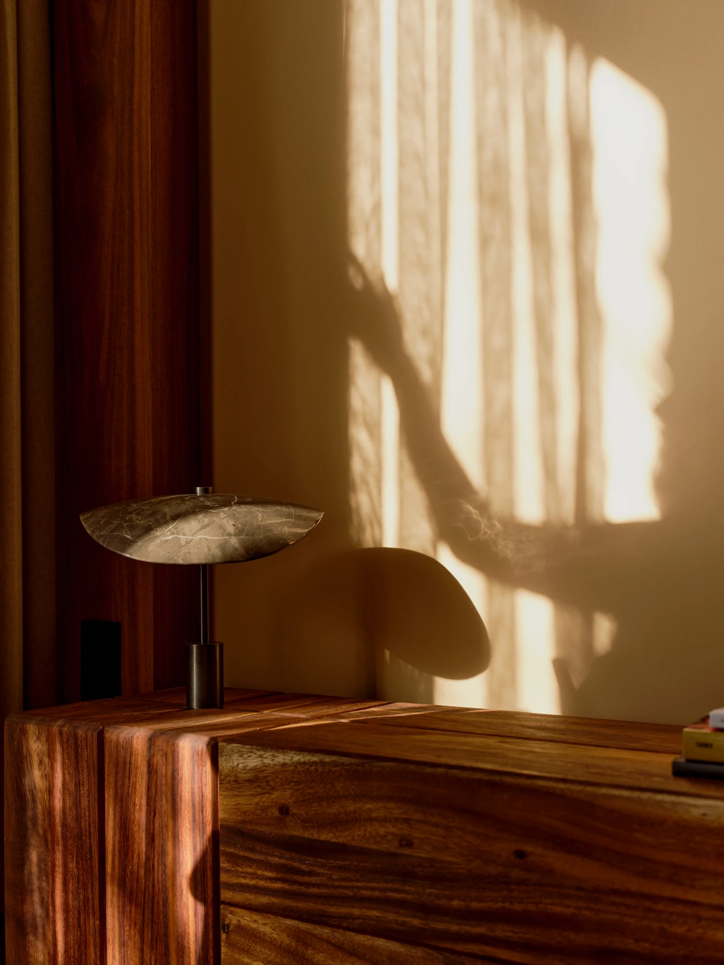 Minimalist table lamp on a wooden console, with warm sunlight casting soft window shadows on the wall.