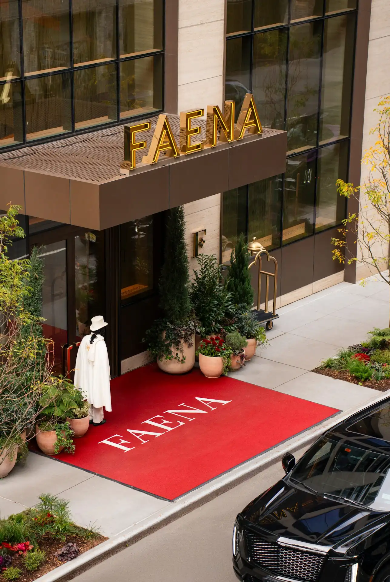 FAENA entrance with red carpet, potted plants, person in white outfit, and parked luxury car.