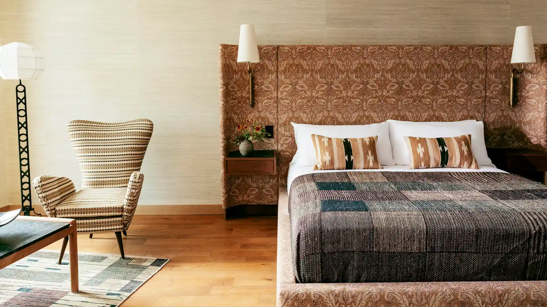 Proper Hotels 5 Stylish bedroom with patterned headboard, geometric pillows, retro armchair, and warm ambient lighting.
