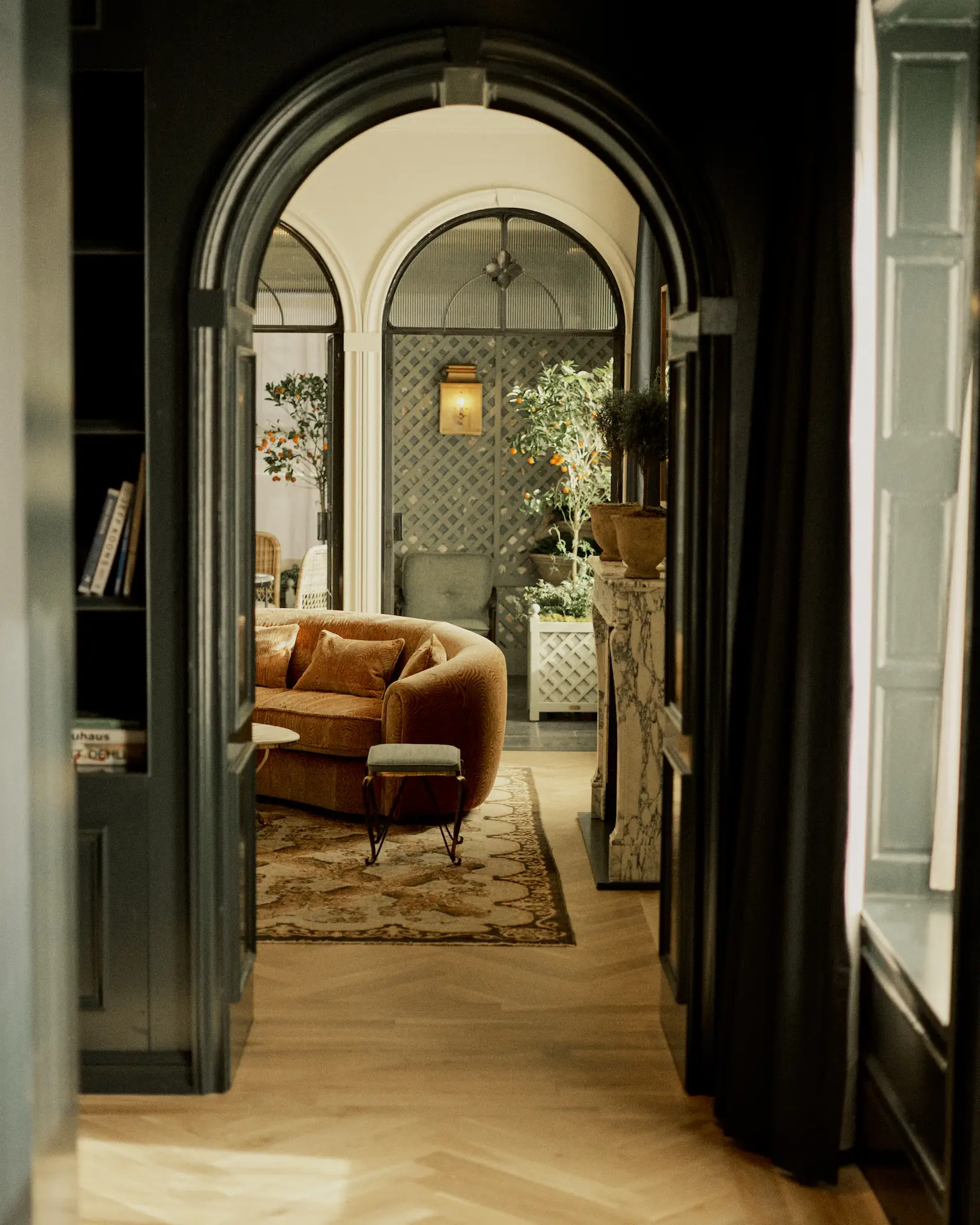 Elegant lounge at The Bellevue Hotel with rust-colored sofa, marble fireplace, and arched windows filtering soft light.