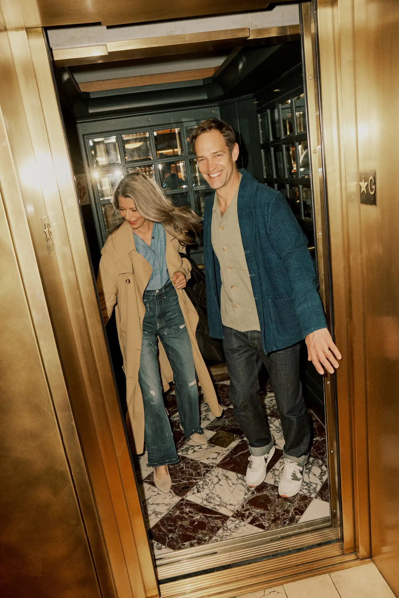 Stylish guests exiting golden elevator at The Bellevue Hotel, marble floor and reflective panels in view.