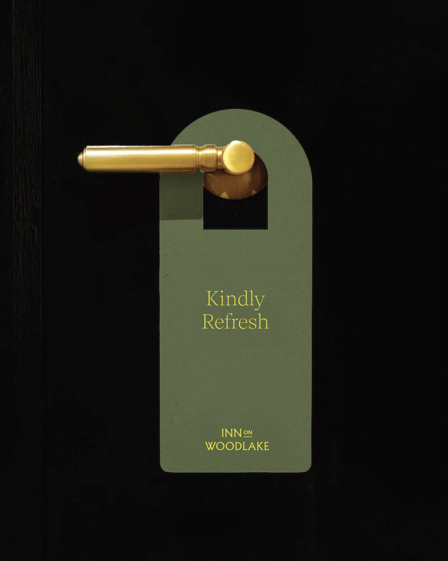 Green “Kindly Refresh” door hanger with yellow text, hanging on gold handle at Inn on Woodlake.