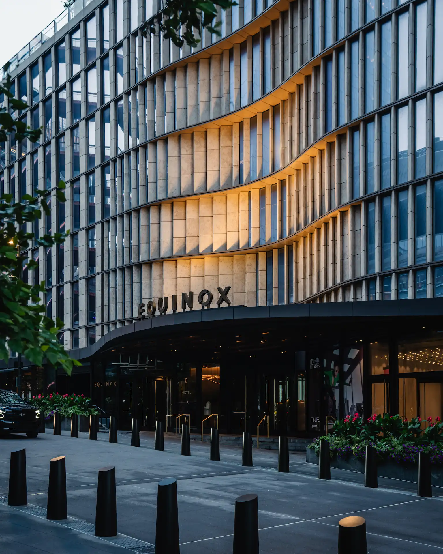 Exterior of Equinox Hotel New York with wave-patterned facade, black awning, and landscaped entrance