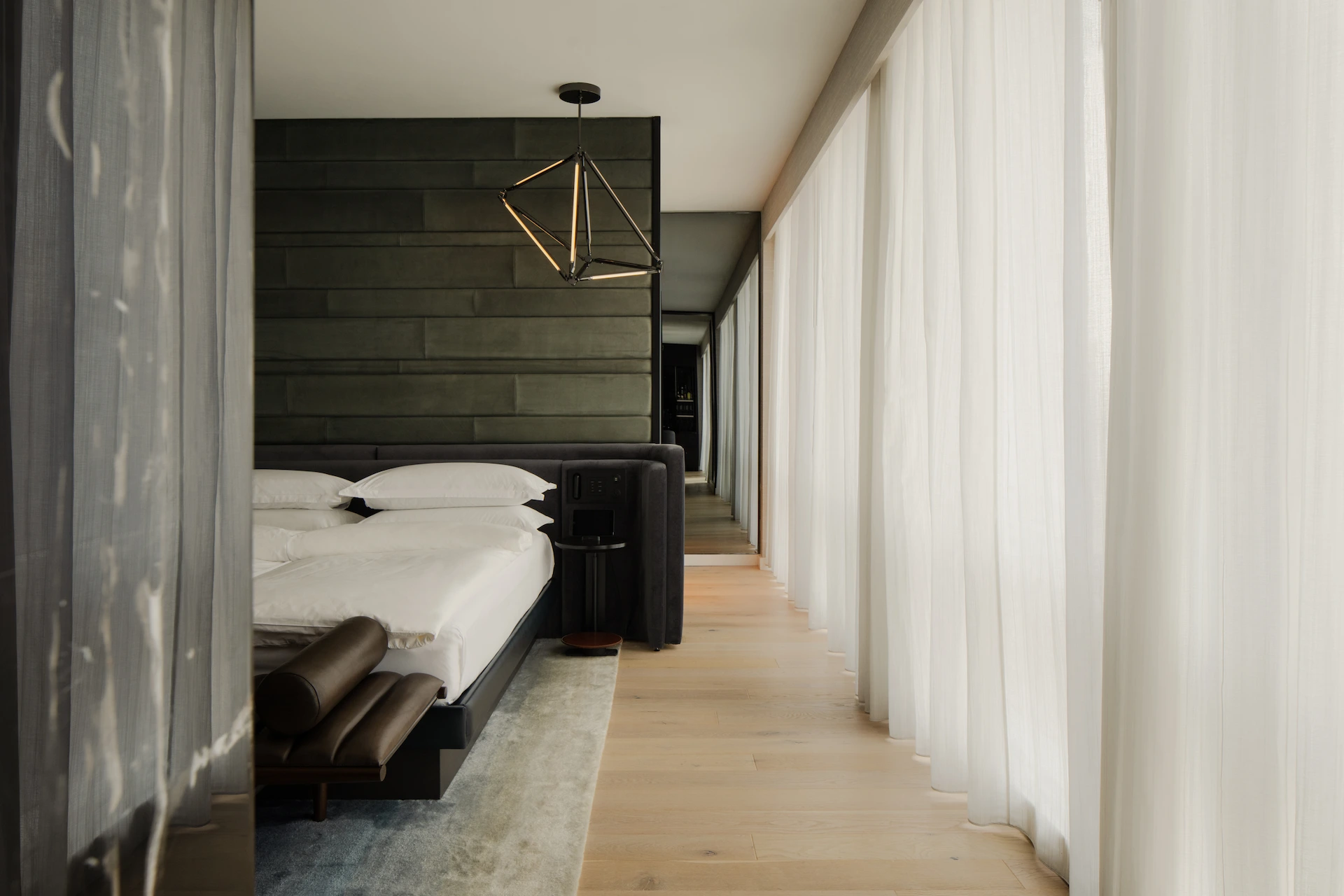 Minimalist bedroom at Equinox Hotel New York with white bedding, geometric pendant light, and sheer curtains