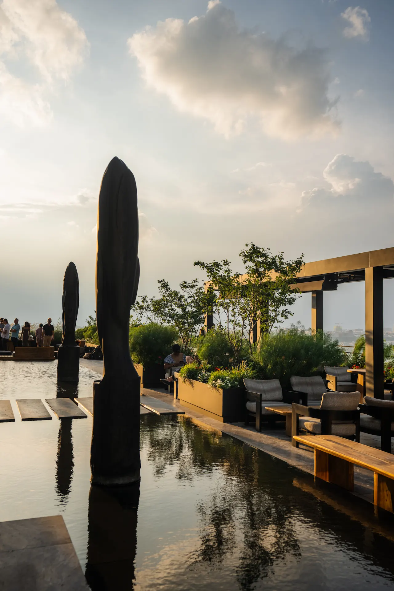 Rooftop sunset scene at Equinox Hotel New York with water feature, sculptures, seating area, and greenery