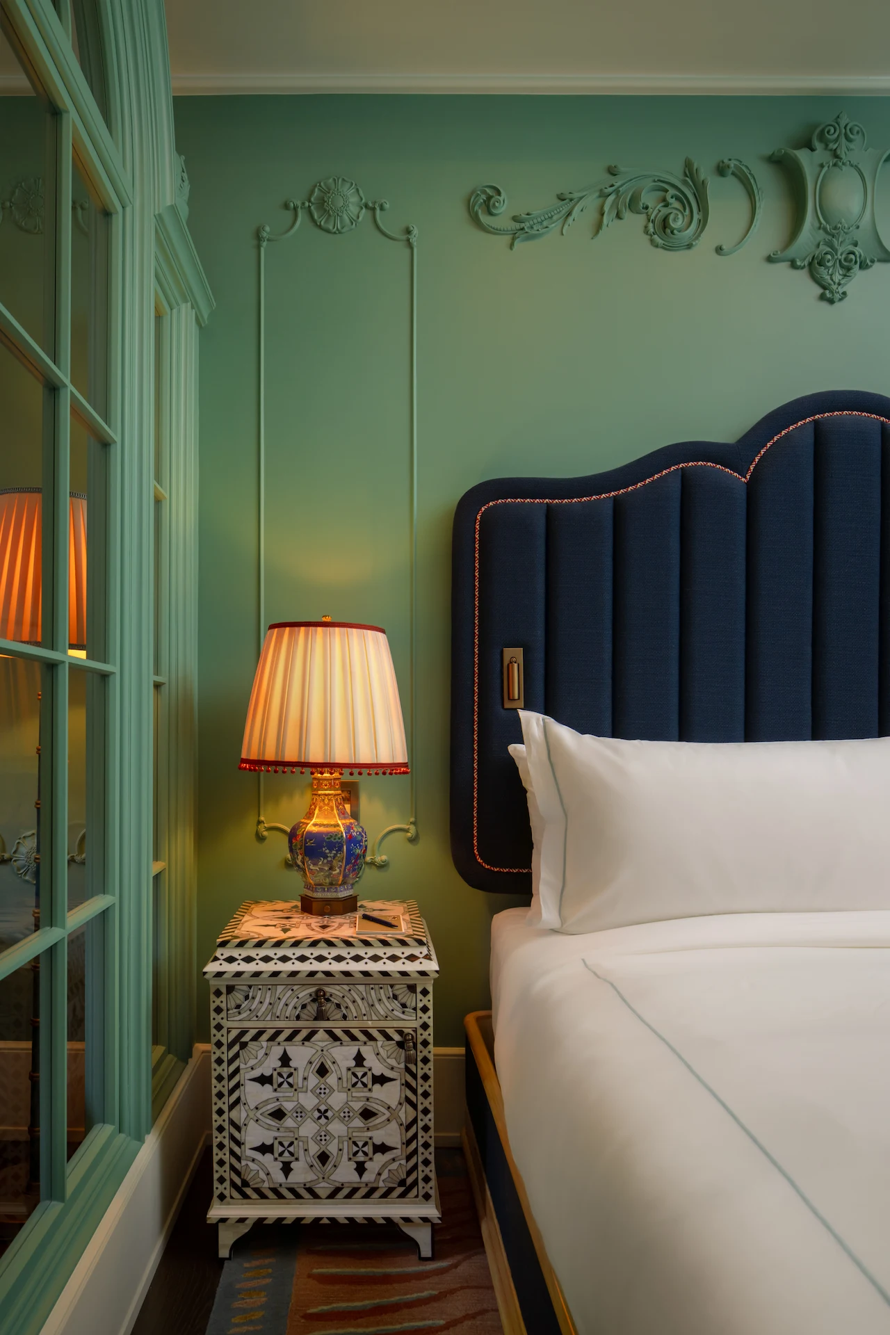 The Fifth Avenue Hotel 4 Bedroom at The Fifth Avenue Hotel with scalloped blue headboard, patterned nightstand, and ceramic lamp
