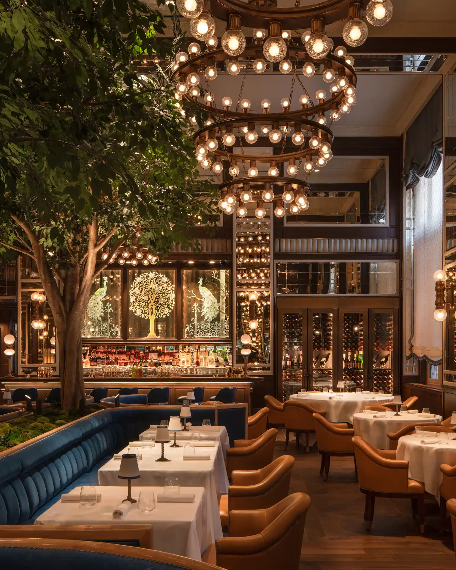 The Fifth Avenue Hotel 1 Elegant restaurant interior with plush seating, white tablecloths, chandelier, and peacock-themed bar