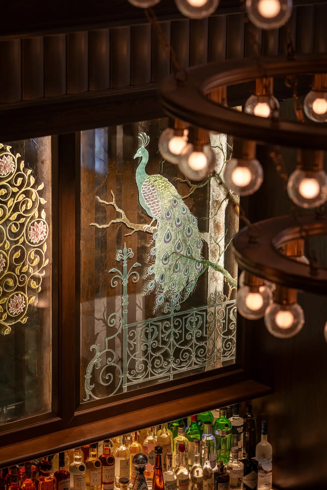 The Fifth Avenue Hotel 2 Stained glass peacock window above chandelier and liquor bottles in elegant bar interior