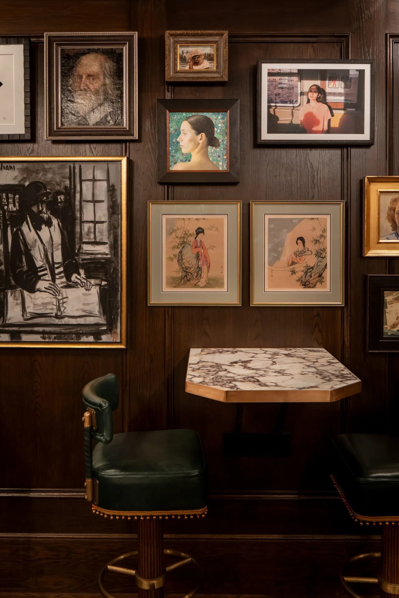 The Fifth Avenue Hotel 3 Dark wood-paneled wall with eclectic framed art above marble table and green leather bar stools