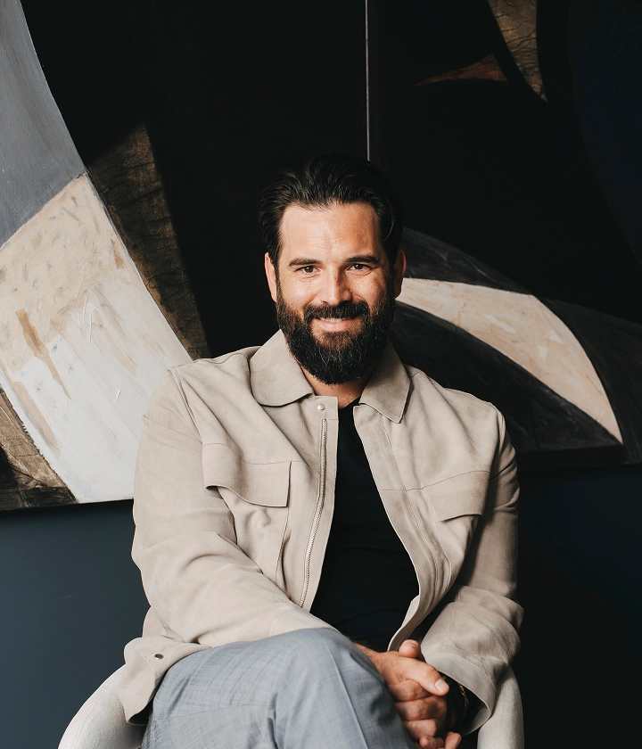 Adam Wallace, Founder & CEO, sits in chair against abstract artwork in neutral tones.