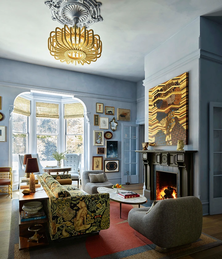 The Madrona 2 Cozy living room with fireplace, patterned sofa, bay window, gallery wall, and sculptural chandelier.