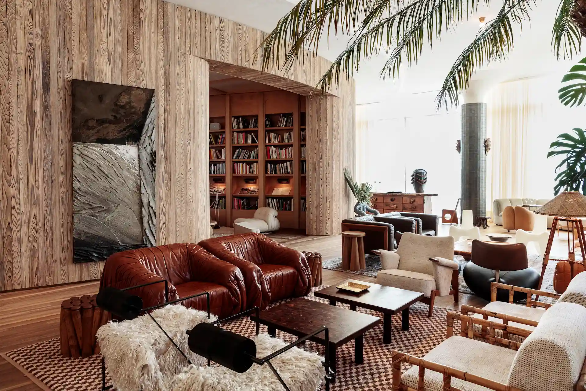 Proper Hotels 2 Eclectic living room with leather and bamboo chairs, patterned rug, large plants, and arched library nook.