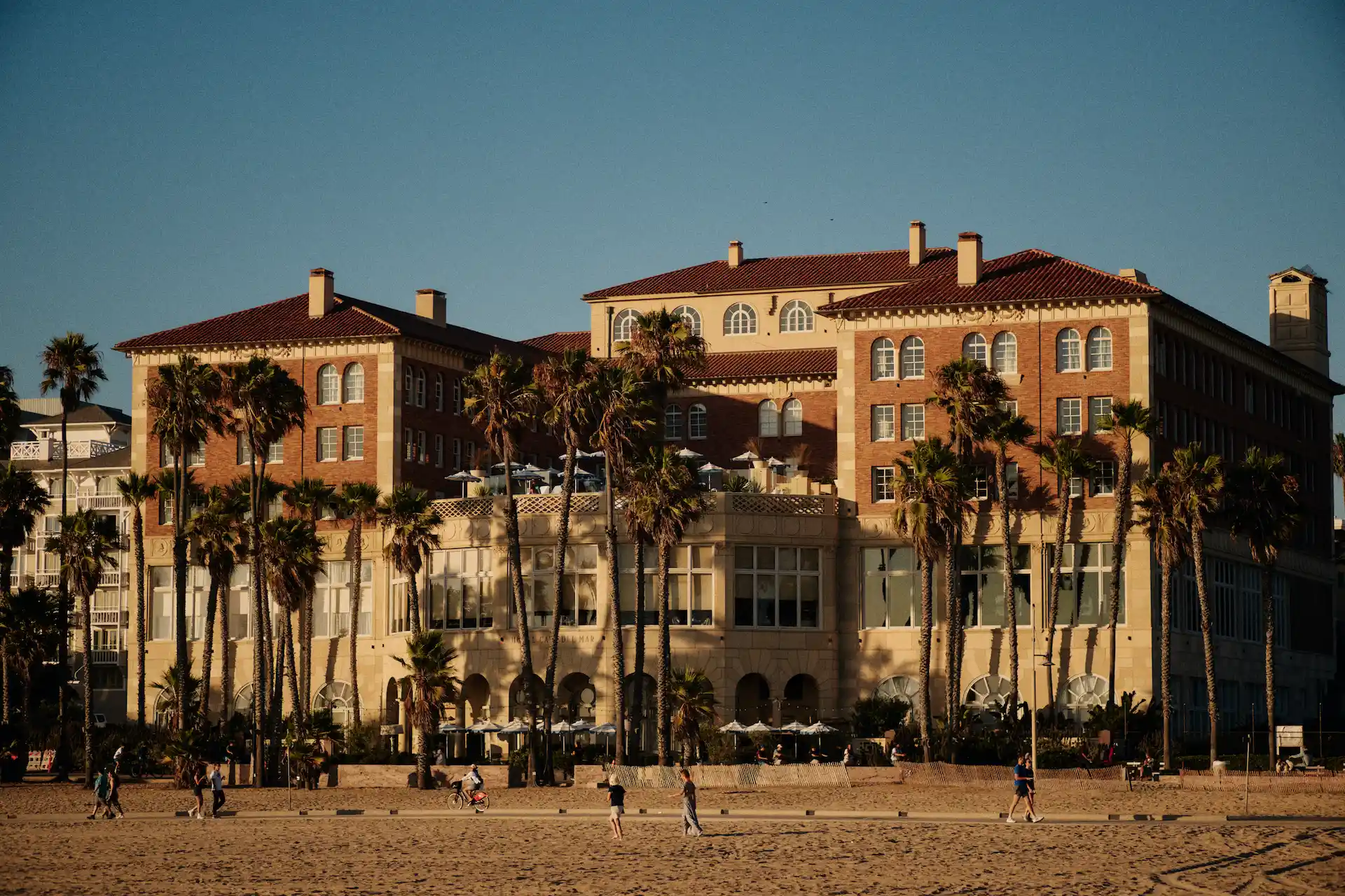 Beachfront view of Casa Del Mar in Santa Monica with Mediterranean architecture, red-tiled roofs, and palm-lined promenade.