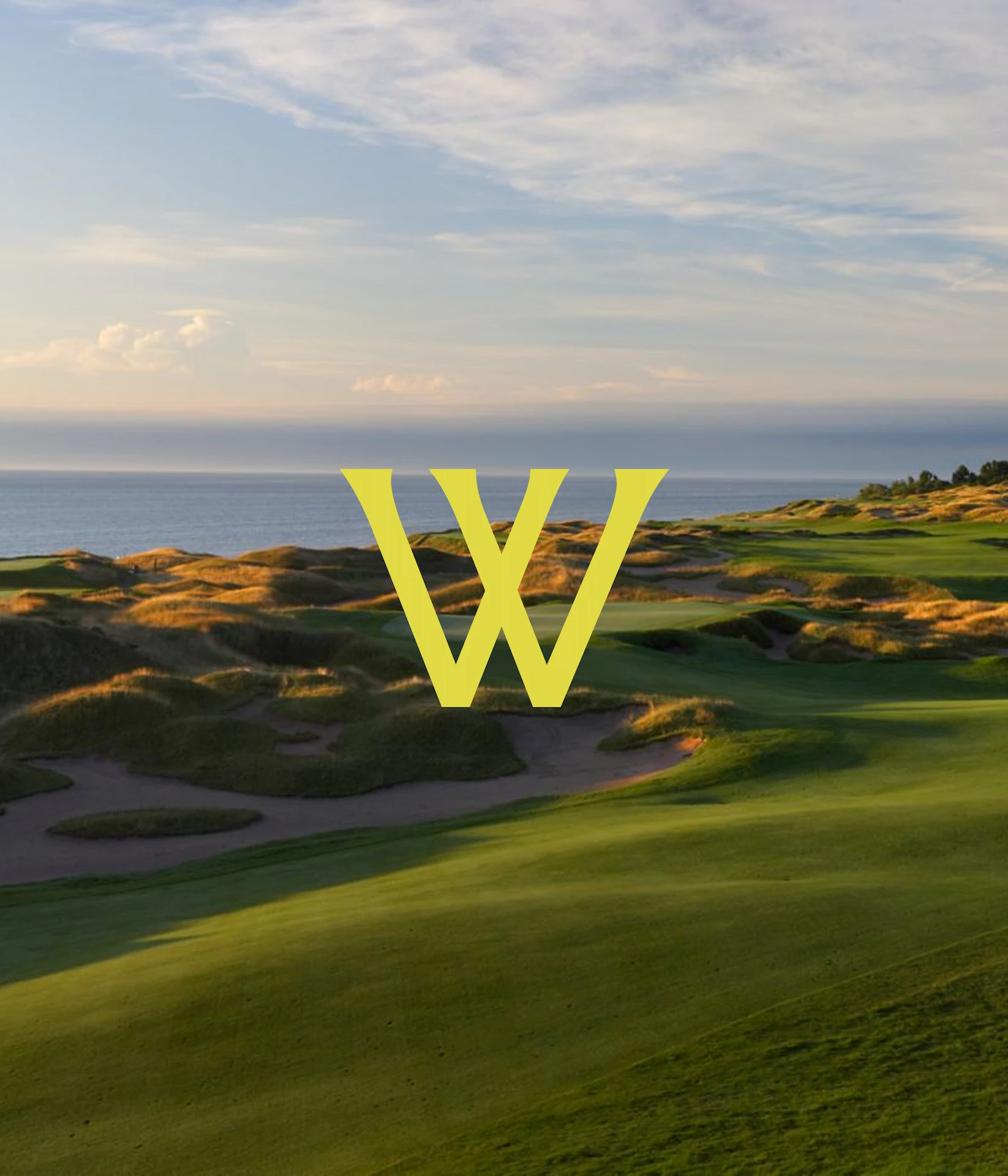 Scenic golf course with rolling green hills, sand bunkers and water view under warm evening light; large yellow “W” centered.