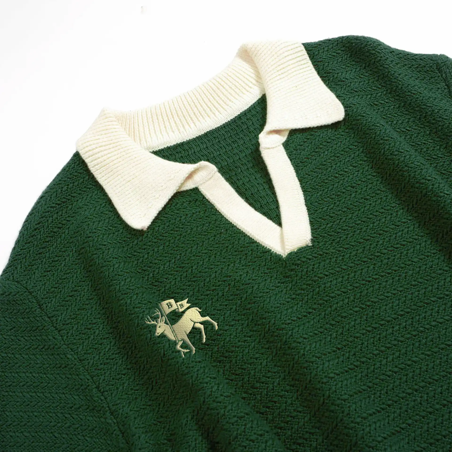 Green knit sweater with cream ribbed collar and embroidered deer carrying “B H” flag on chest.
