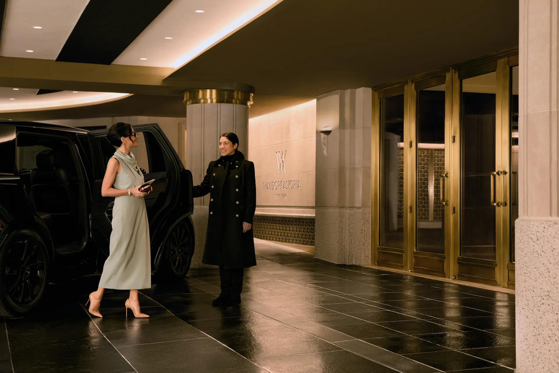 Guest exiting a luxury SUV at a hotel entrance, greeted by staff beneath warm lighting and gold-accented doors.
