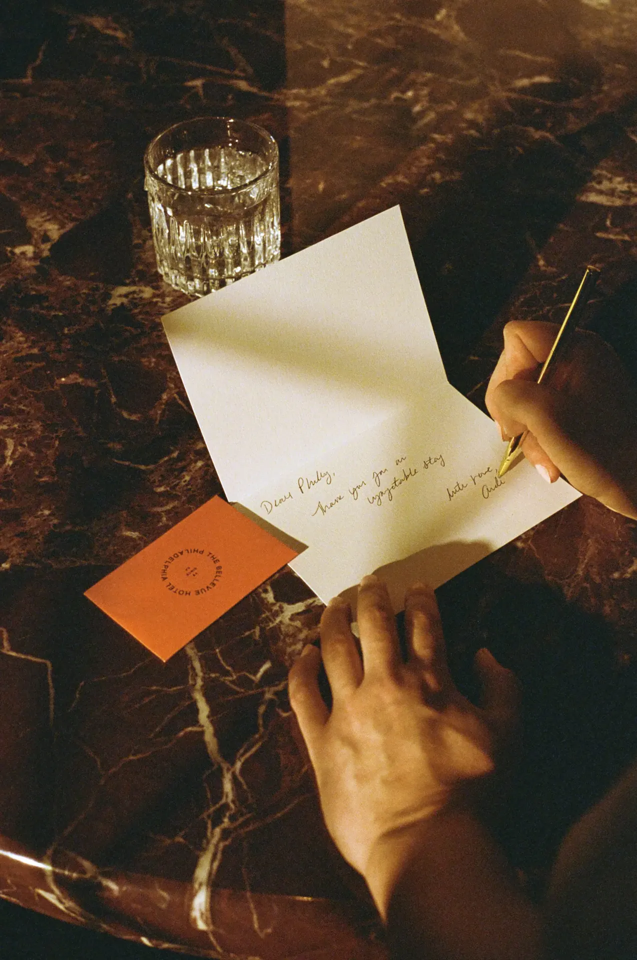 Handwritten thank-you note on marble surface with gold pen, glass of water, and Bellevue Hotel envelope.
