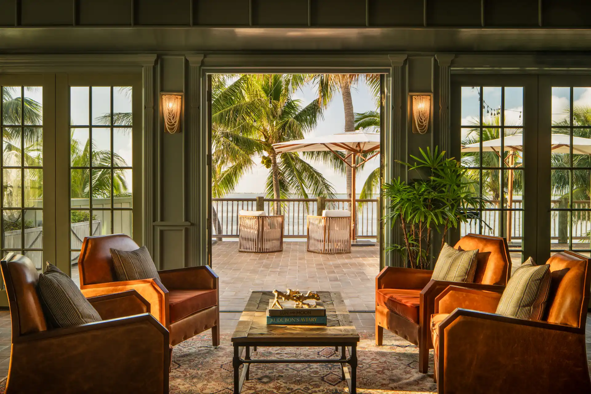 Elegant hotel lounge with leather chairs opening to a palm-lined terrace and ocean view.