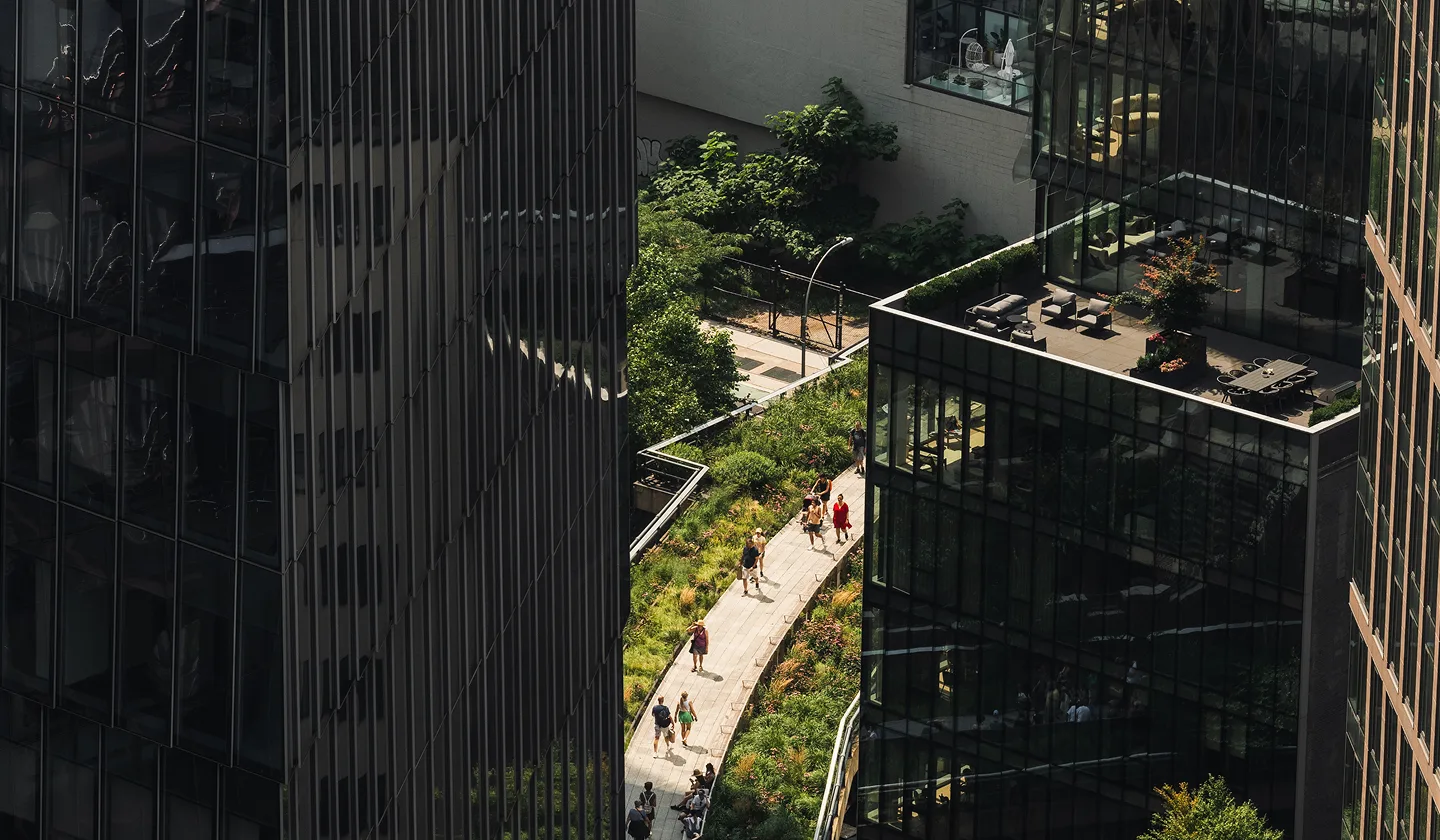 Pedestrians walking along elevated green walkway between modern glass office buildings.