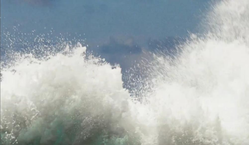 Ocean waves crashing with white spray against a blue sky, capturing motion and sea mist in bright daylight.