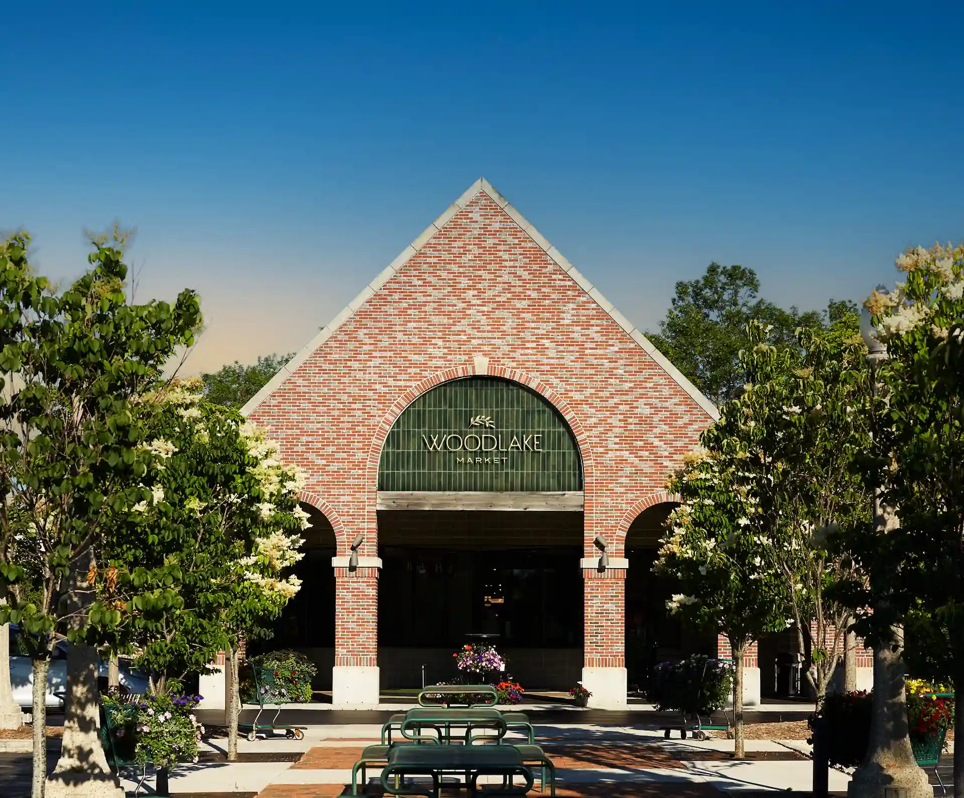 Woodlake Market 1 Front entrance of Woodlake Market with red brick gable, green signage, arched entryways, and outdoor seating.