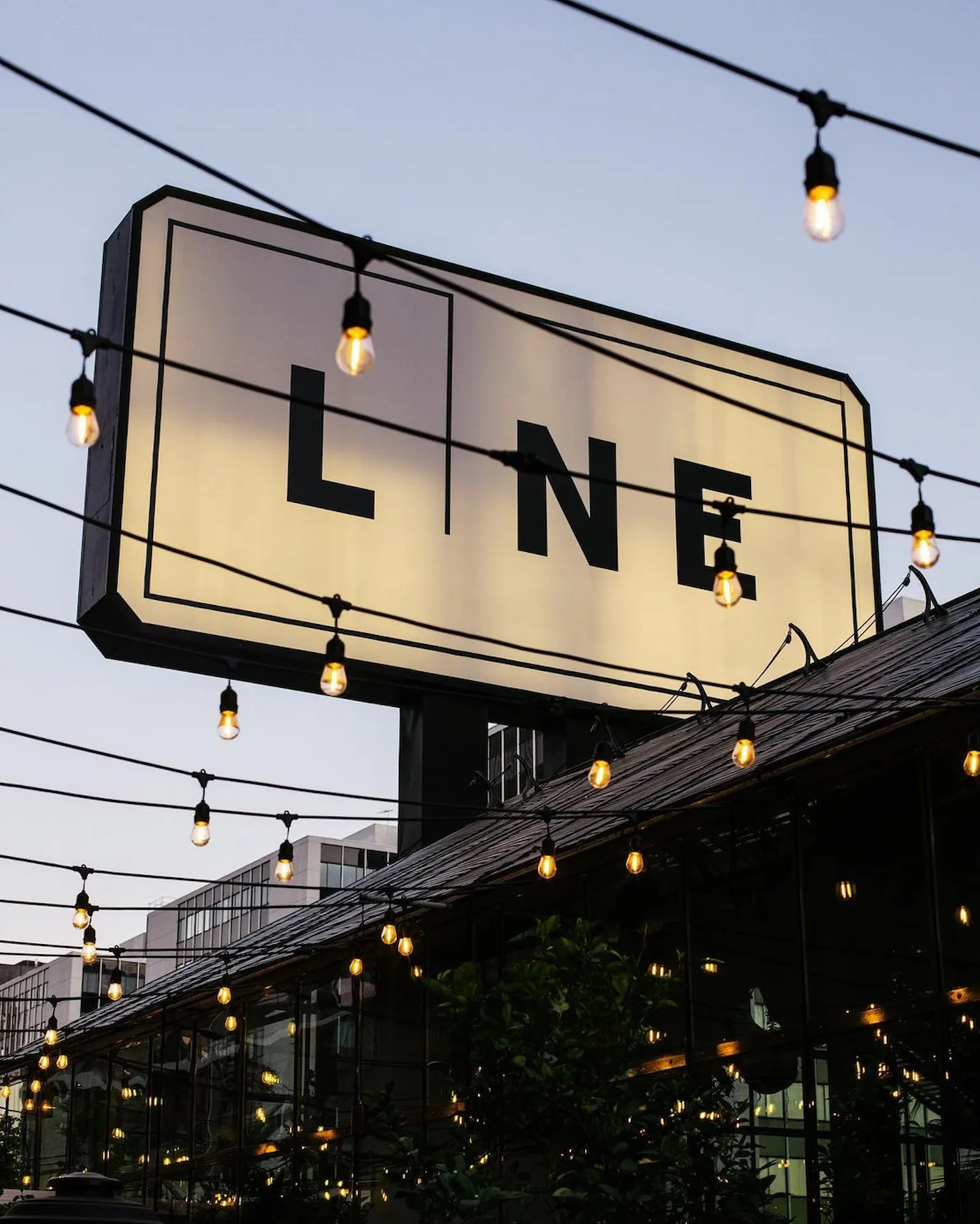 The LINE 2 Large illuminated The LINE hotel sign with hanging string lights at dusk
