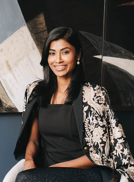 Biby Notten, VP Client Relations, seated in embroidered jacket with abstract artwork in background.