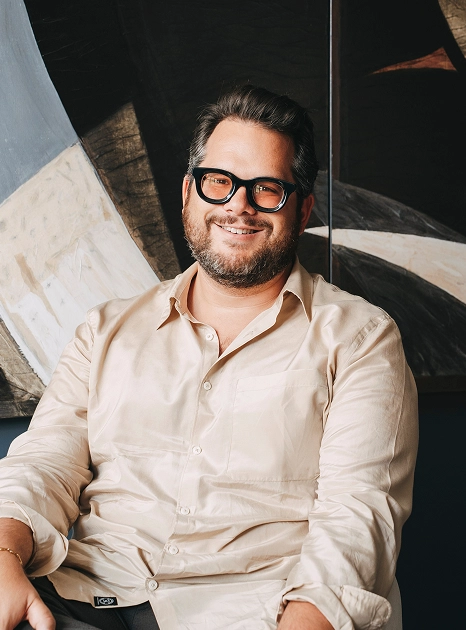 Ernest Wlostowski, head of creative, seated in beige shirt with abstract artwork in background.